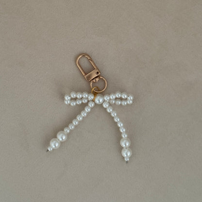 Pearl bow keychain on a beige surface